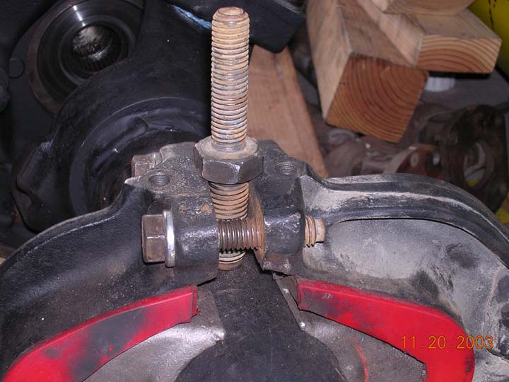 Threaded spreader tool bolted across a black differential housing with red parts below