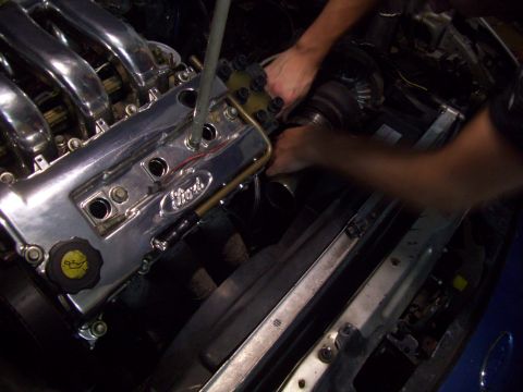 1995 Ford Probe - Hands work on engine components in a vehicle's engine bay, focusing on a chrome valve cover.