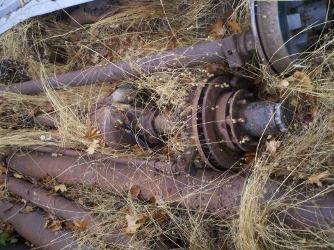 1978 Ford Bronco - Discarded vehicle parts, including axles and brake rotors, lie in a grassy, outdoor setting.
