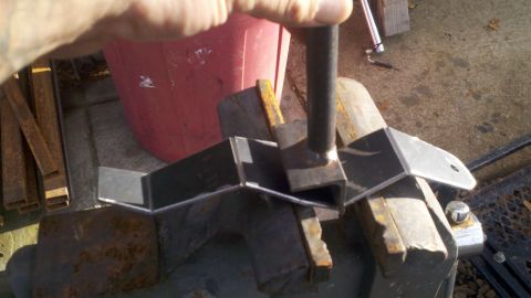 1978 Ford Bronco - A metal bracket is being worked on in a vise, with a red container visible behind it.