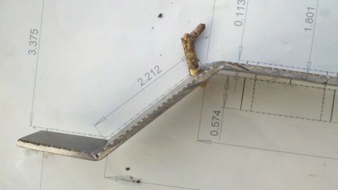 1978 Ford Bronco - A metal bracket with a twig attached is shown against a blueprint with measurements.