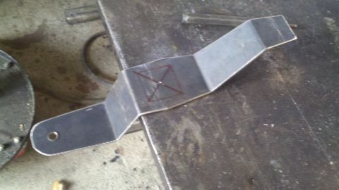 1978 Ford Bronco - Custom metal bracket with scribe marks for drilling, resting on a workbench.