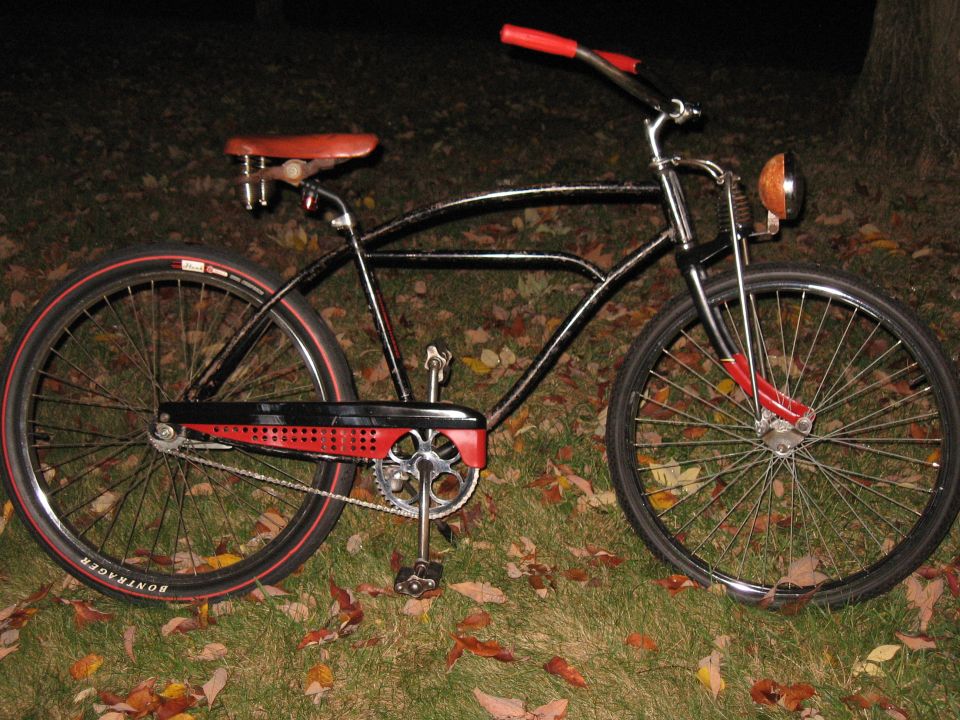 Black cruiser bicycle with red handlebars and seat, chrome accents, and a red chain guard
