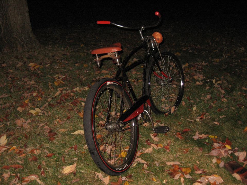 black cruiser bike with red handlebars and seat, parked on grass with fallen leaves
