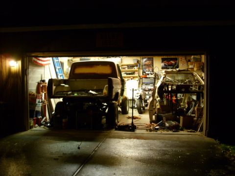 1967 Ford F-250 - Two vehicles, a pickup truck and a car chassis, are in a garage with tools and equipment.