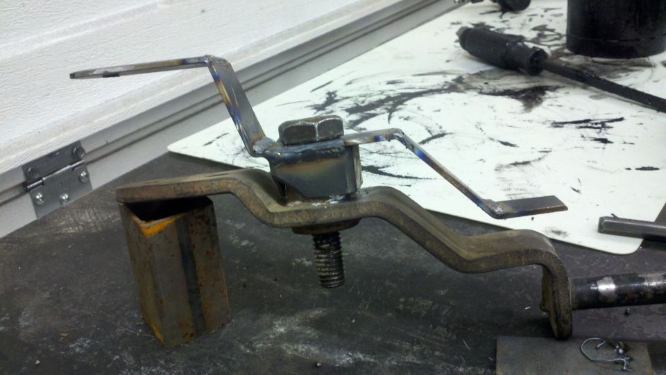 Custom welded metal bracket with a bolt and nut assembly, resting on a workbench