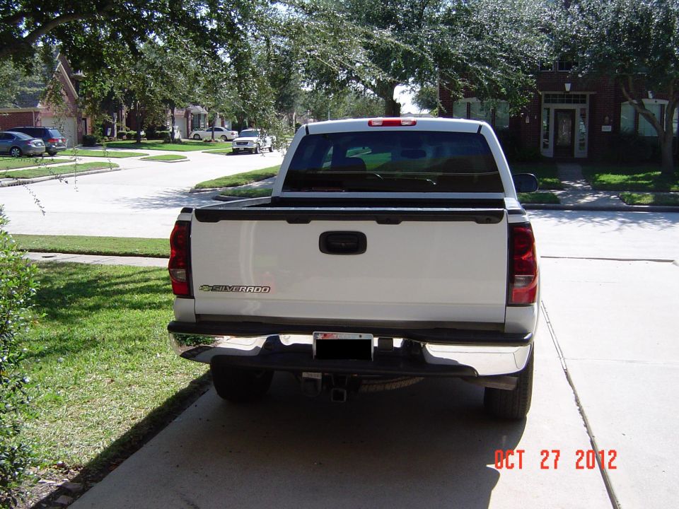White pickup truck parked in a driveway, rear view. Suburban neighborhood in background