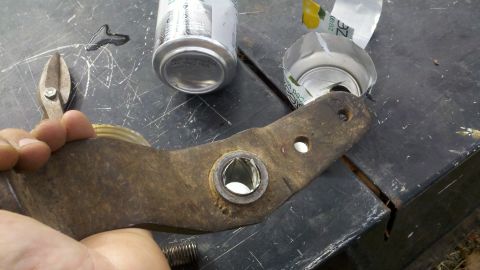 1978 Ford Bronco - A rusty metal part is held in a hand, with two opened cans nearby on a workbench.