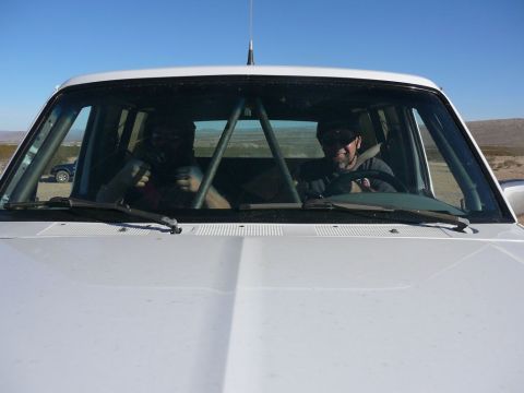 1988 Ford Bronco - Two people inside a 1988 Ford Bronco with a roll cage, desert landscape visible through windows.