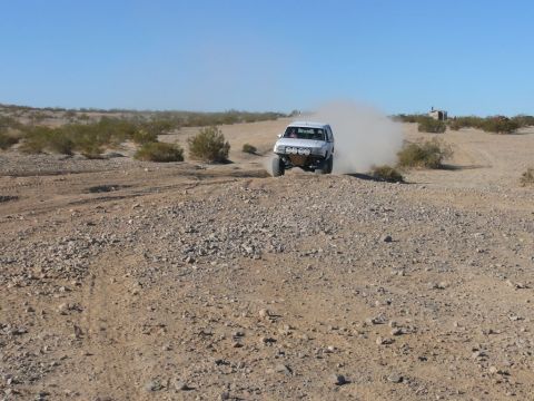 1988 Ford Bronco - A white off-road SUV drives through a dusty desert landscape.