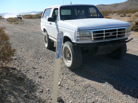 1988 Ford Bronco - A white 1992 Ford Bronco navigates a dusty desert road, passing a course marker.