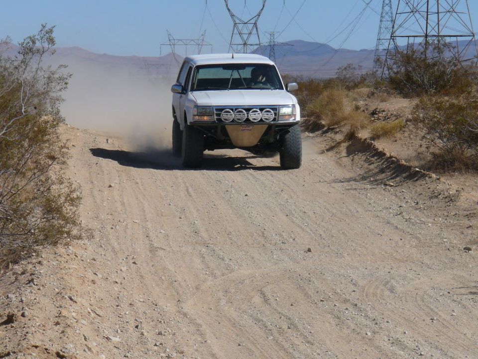 White SUV with off-road lights and bumper driving on a dusty desert road