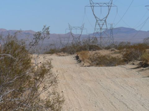 1988 Ford Bronco - A dirt road winds through a desert landscape with large power line towers in the distance.