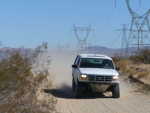 1988 Ford Bronco - A white 1992 Ford Bronco navigates a dusty desert road, with power lines visible in the background.