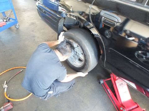 2003 Ford Crown Victoria - Rear-quarter view as a kneeling worker positions a smooth drag tire under the fender of a black car on a jack.
