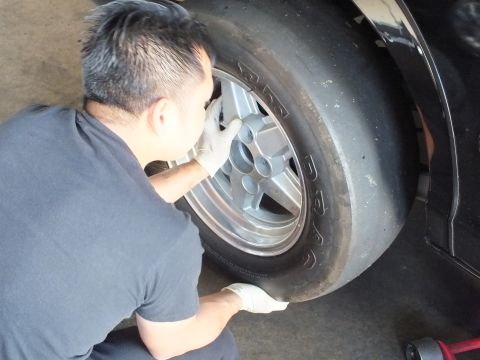 2003 Ford Crown Victoria - Worker grips a polished five-spoke wheel wrapped in an M&H drag slick beside the black sedan's wheel arch.