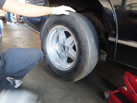 2003 Ford Crown Victoria - balding drag slick on a polished aluminum wheel is lifted into the rear wheel well of a black sedan.