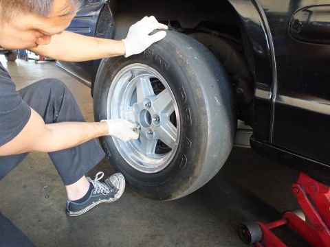 2003 Ford Crown Victoria - Technician aligns a wide drag slick and five-spoke wheel against the rear wheel arch of a black car.