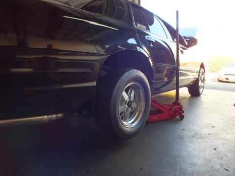 2003 Ford Crown Victoria - Ground-level shot of a black sedan's rear corner lifted on a jack, fitted with a five-spoke aluminum drag wheel.