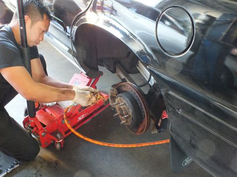 2003 Ford Crown Victoria - Sparks fly as a technician grinds the rear hub of a black Ford sedan beside a Ford-branded mud flap.
