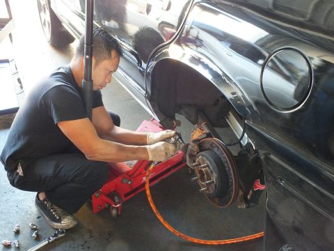 2003 Ford Crown Victoria - Worker grinds at the rear brake of a black car raised on a red jack, sparks beside the exposed hub.