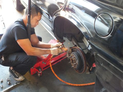 2003 Ford Crown Victoria - Sparks fly from a grinder at the rear brake drum of a black sedan on a jack, exposed hub in view.
