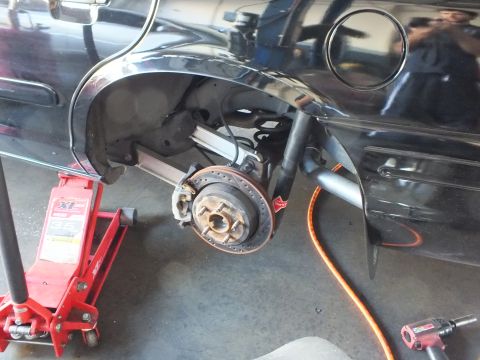 2003 Ford Crown Victoria - Close view of a black sedan's bare rear hub and brake assembly with the wheel removed, jacked in a garage.
