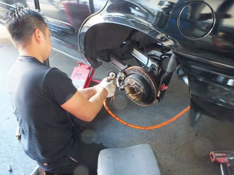 2003 Ford Crown Victoria - Worker tends the bare rear hub of a black car on a jack, a drag wheel resting beside the open wheel well.