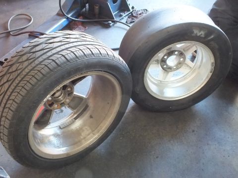2003 Ford Crown Victoria - Two polished aluminum wheels lie on a shop floor, one with a treaded street tire, one with a wide M&H slick.