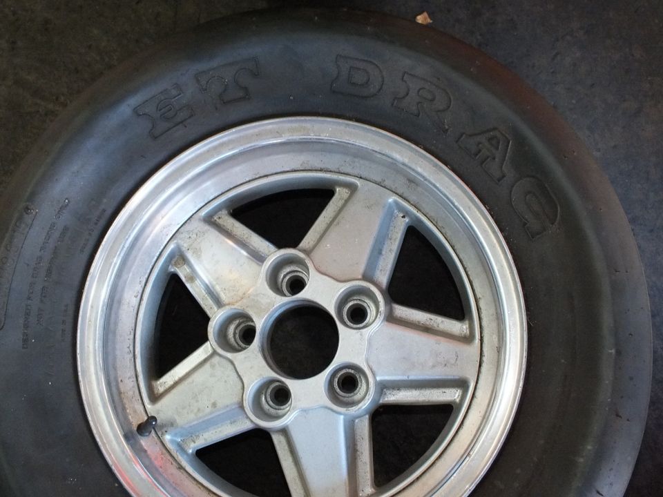 Polished five-spoke aluminum wheel with five-lug pattern wrapped in M&H ET Drag slick on floor