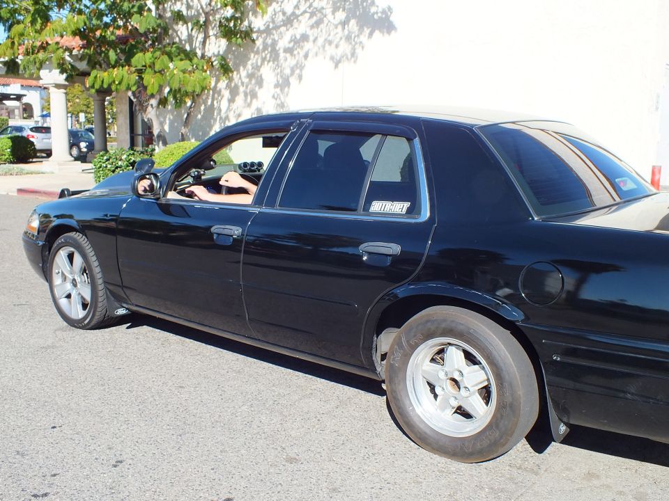 Black Ford Crown Victoria sedan side view with skinny front drag tire and 5-spoke wheel
