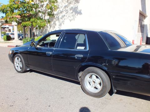 2003 Ford Crown Victoria - Lowered black four-door against a stucco wall, mismatched drag-style front and rear tires.