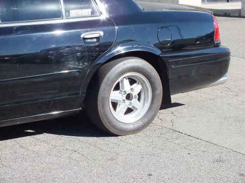 2003 Ford Crown Victoria - Close detail of a wide rear drag tire and aluminum wheel under a black sedan body.