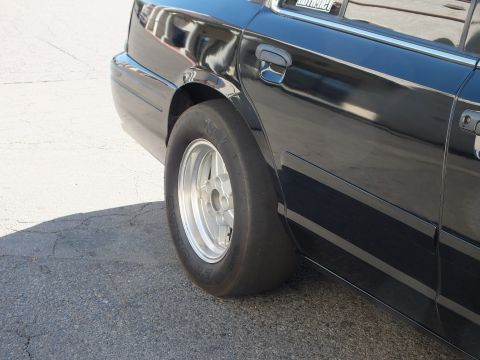 2003 Ford Crown Victoria - Narrow front runner tire and door handle of a black four-door over pavement.