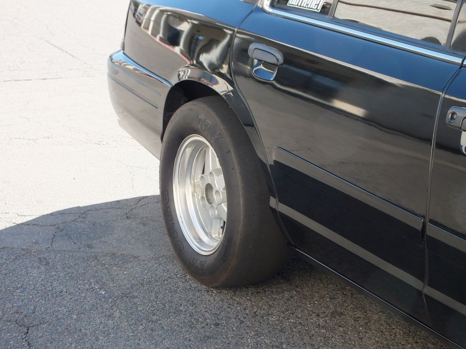 Front skinny drag tire on polished wheel and black fender of full-size sedan