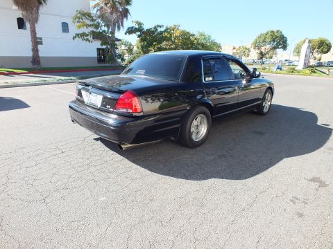 2003 Ford Crown Victoria - Rear quarter of a lowered black four-door with aftermarket wheels in an empty lot.