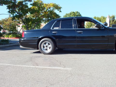 2003 Ford Crown Victoria - Side view of a black four-door with a driver visible, front runner tire turned out.