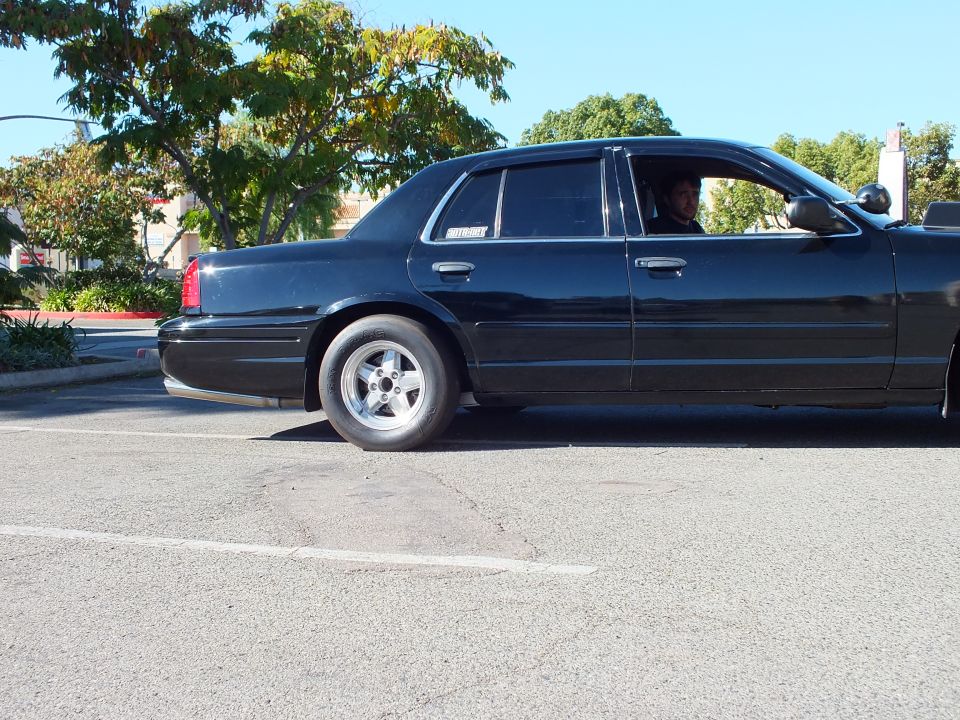 Black Ford Crown Victoria driver side with man inside and narrow front tire