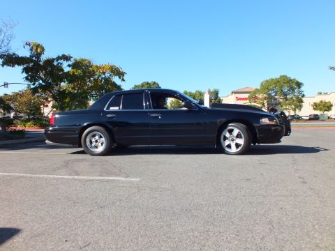 2003 Ford Crown Victoria - Lowered black four-door on staggered wheels parked under clear blue sky.