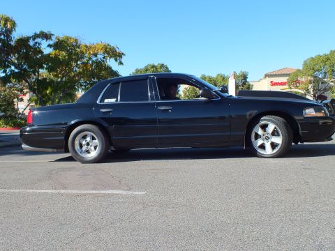 2003 Ford Crown Victoria - Driver profile of a black sedan with staggered wheels and a SuperMotors window decal.