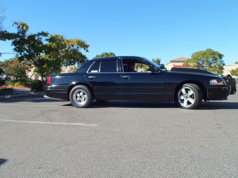 2003 Ford Crown Victoria - Full passenger-side view of a lowered black four-door against blue sky.