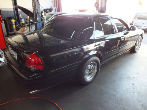 2003 Ford Crown Victoria - Black four-door parked in a garage bay showing tail light and drag wheel.