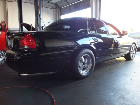 2003 Ford Crown Victoria - Black four-door in a shop bay with hood raised and rear tail light lit by daylight.