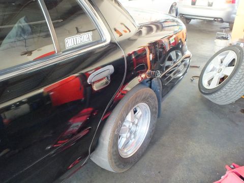 2003 Ford Crown Victoria - Black four-door door and rear tire reflecting shop lights, alloy wheel beside it.