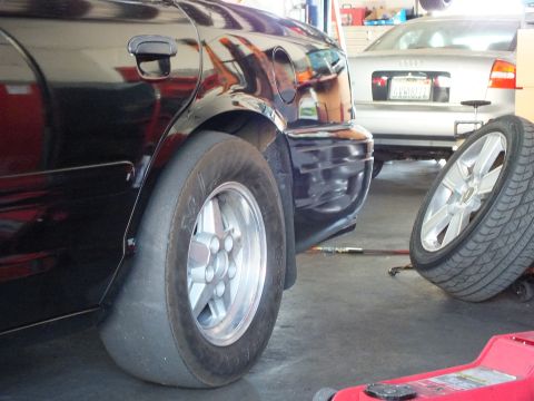 2003 Ford Crown Victoria - Wide rear drag tire and wheel tucked under a black sedan fender inside a garage.