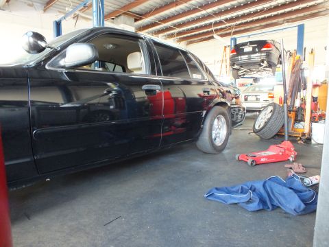 2003 Ford Crown Victoria - Lowered black four-door beside a floor jack and shop rags with a lifted car behind.