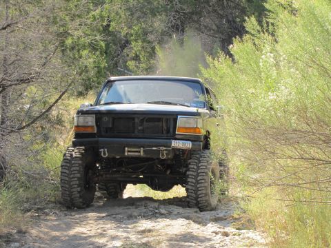 1995 Ford Bronco - This lifted 1995 Ford Bronco navigates a dusty trail surrounded by vegetation.