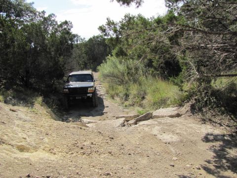 1995 Ford Bronco - 1995 Ford Bronco navigating a challenging off-road trail with rocky terrain.