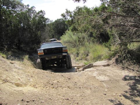 1995 Ford Bronco - This lifted truck navigates a challenging off-road path with another vehicle following closely behind.