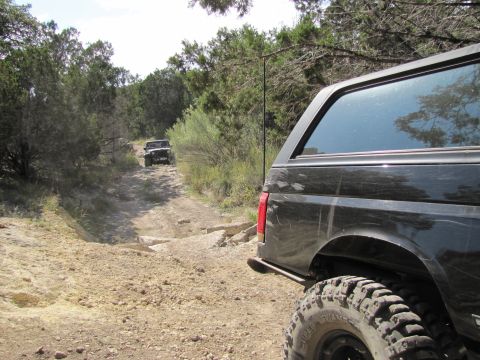 1995 Ford Bronco - Two SUVs navigate a rocky off-road trail through a wooded area.